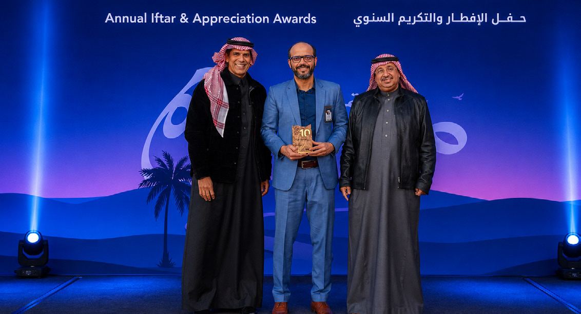 An honouree holding the Masira trophy between two colleagues on stage